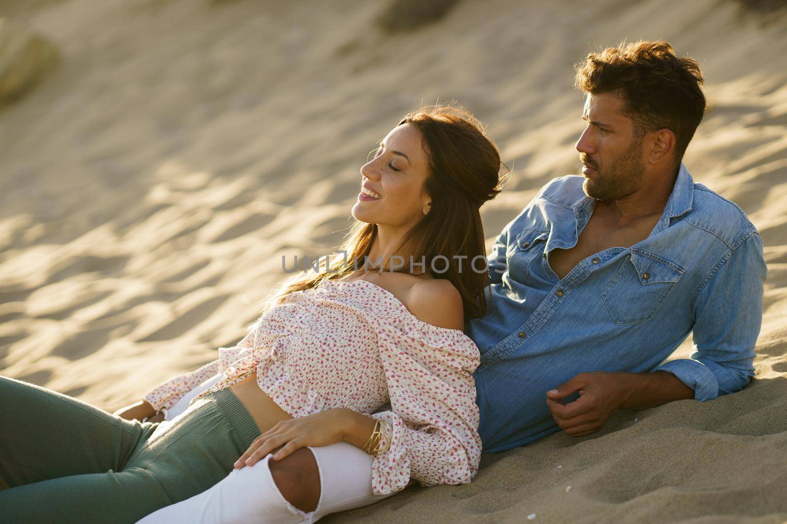 Happy loving couple sitting on the sand of the beach enjoying each other