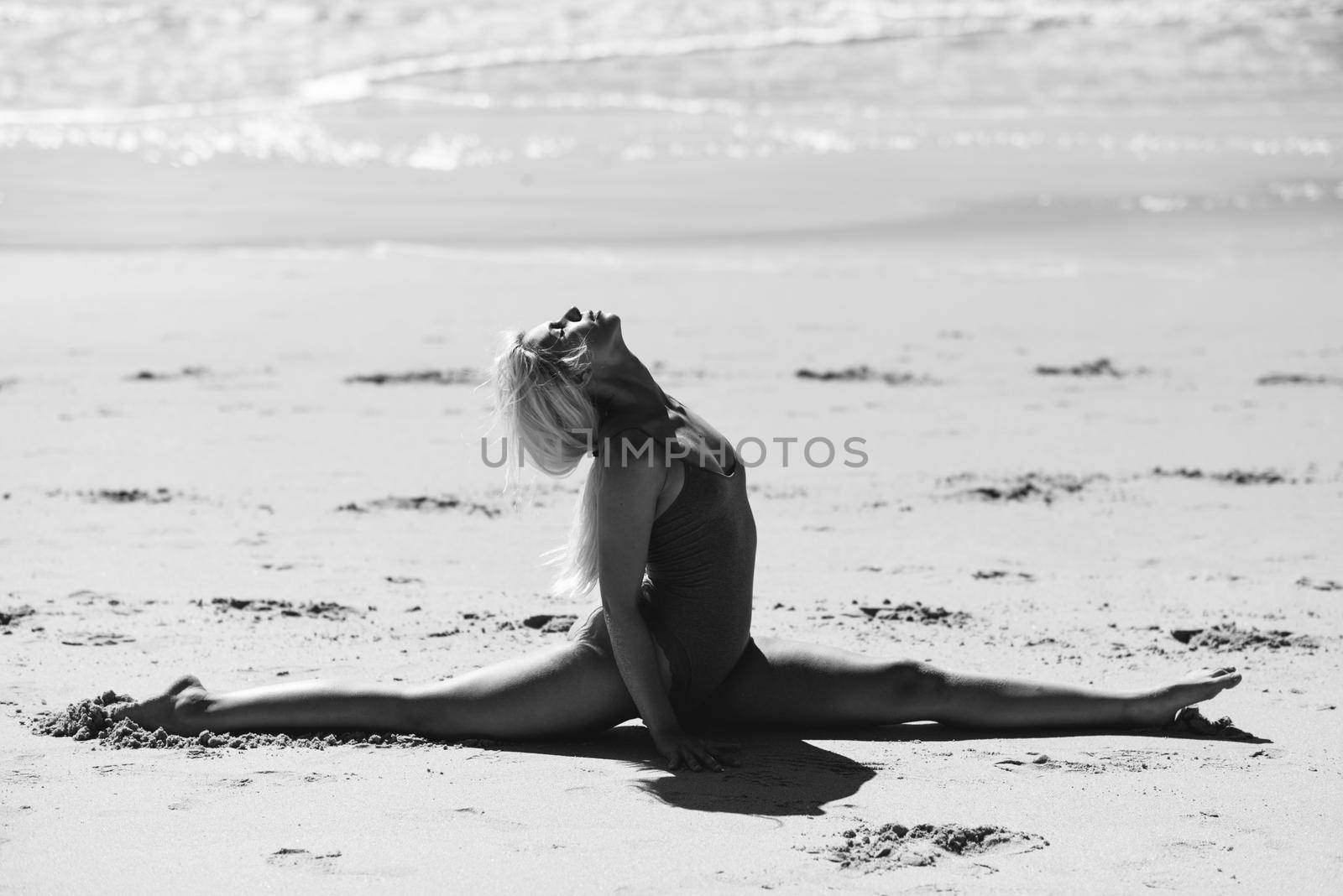 Caucasian woman practicing yoga at seashore. Young female doing fitness legs split on sand in the beach in Cadiz, Andalusia, Spain.