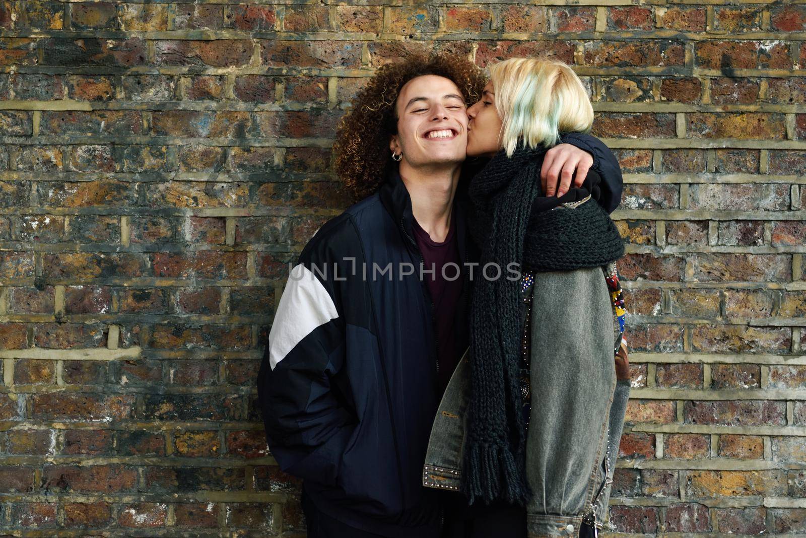 Young couple enjoying Camden town in front of a brick wall typical of London, UK. Man and woman kissing