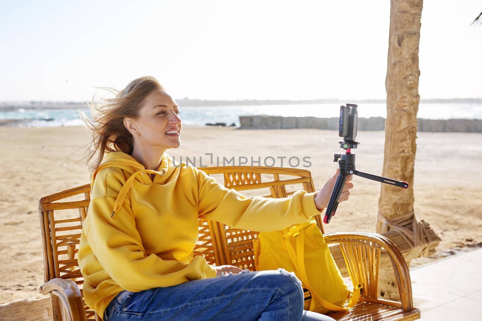 Technology, lifestyle, leisure and travel. Middle-aged female making online video call talking laughing, using smartphone, sunset seascape, sandy beach background, tropical autumn winter spring season