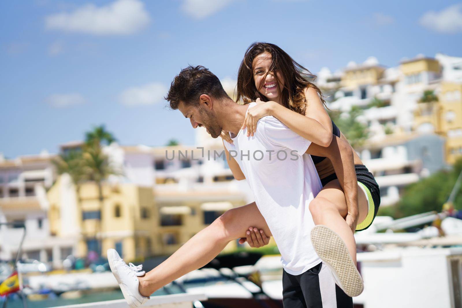 Man carrying his girlfriend on piggyback wearing sport clothes. by javiindy