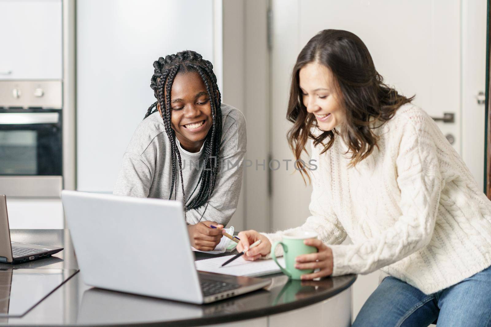 Two college girls studying together at home with laptops while drinking coffee by javiindy