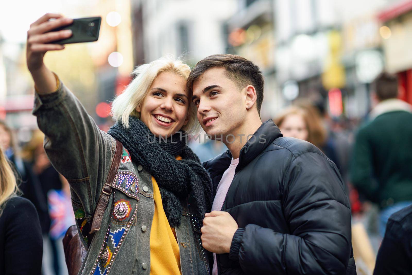 Happy couple of tourists taking selfie in a crowded street. by javiindy