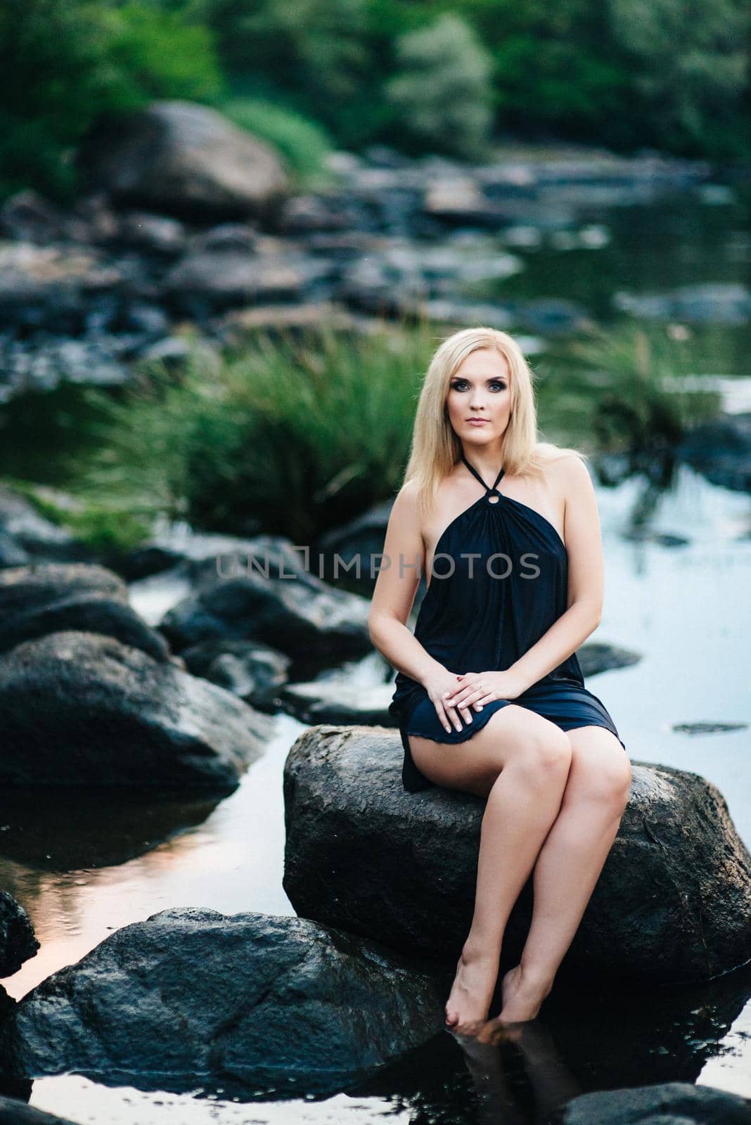 blonde girl in a black dress with blue eyes on the stone coast of the river