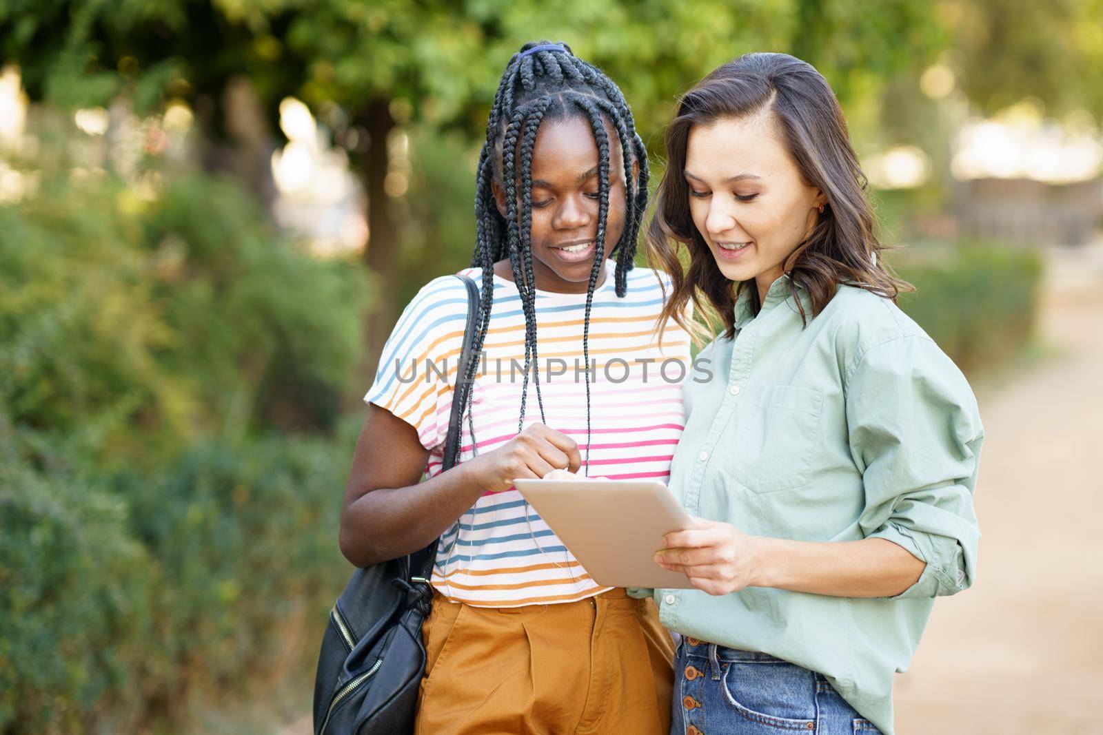 Two multiethnic women consulting something on a digital tablet outdoors.