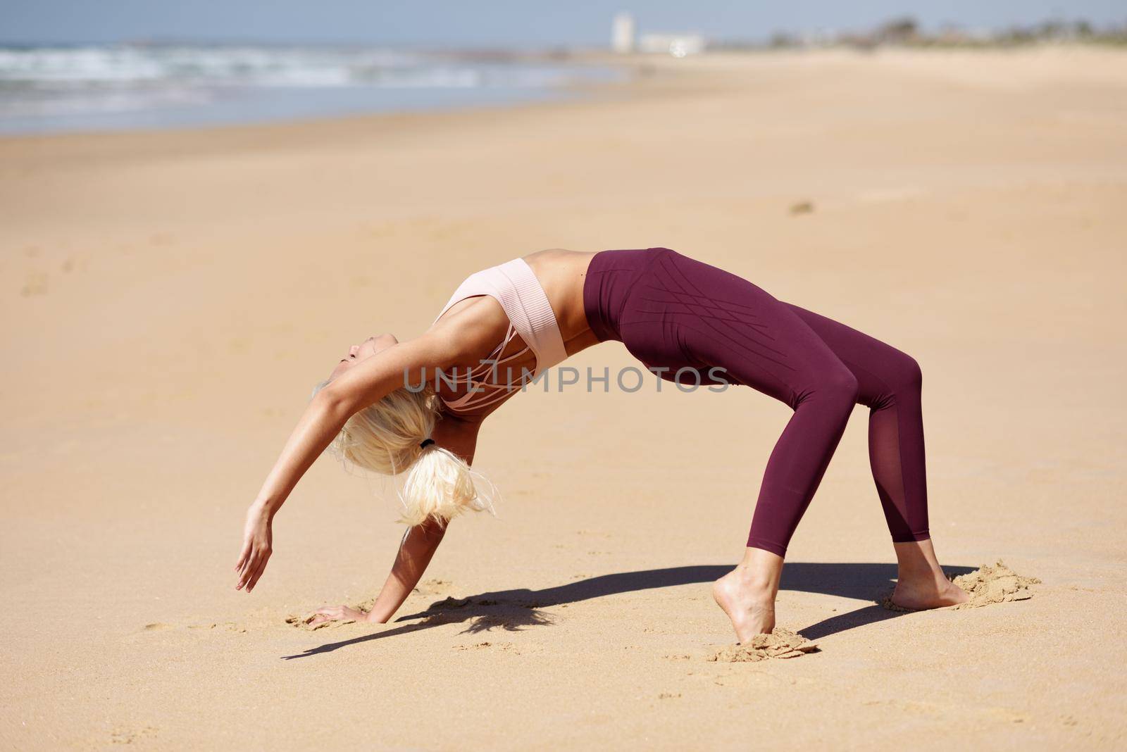 Caucasian blonde woman practicing yoga in the beach by javiindy