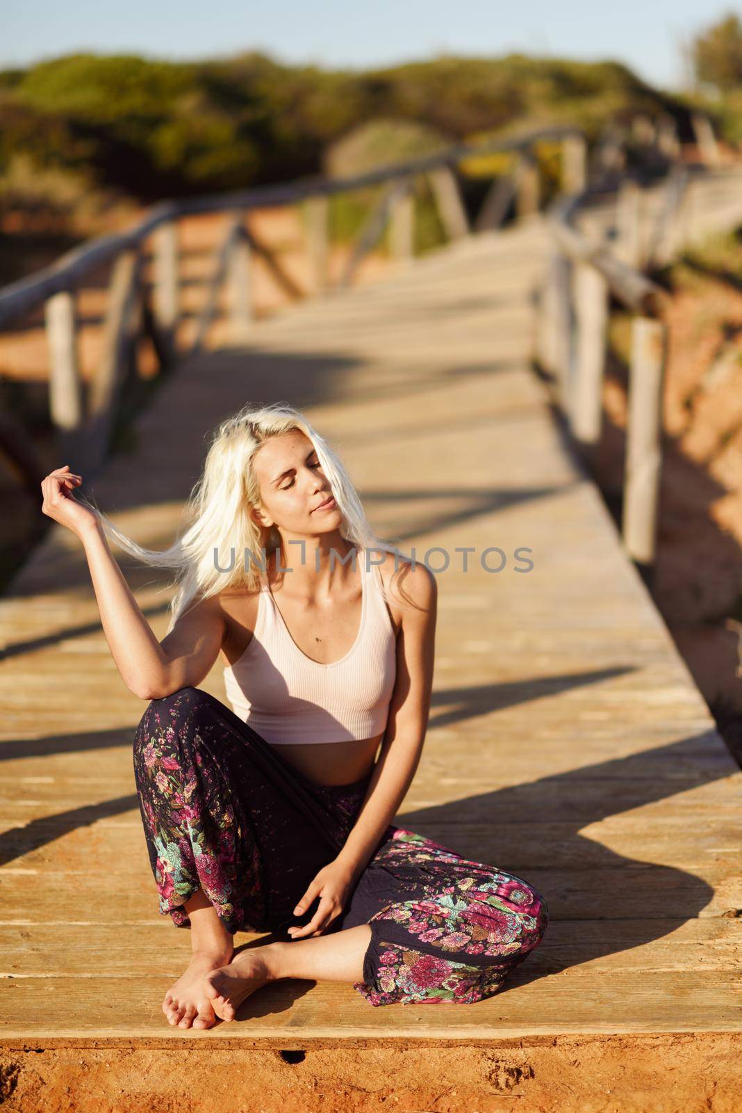 Woman enjoying the sunset on a beautiful beach in Cadiz, Andalusia, Spain. Young female smiling sitting on wooden bridge.