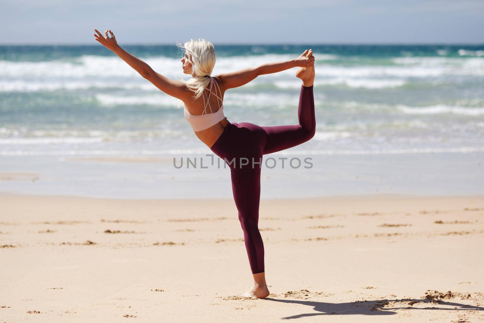 Caucasian woman practicing yoga at seashore. Young female raising arms in the beach in Cadiz, Andalusia, Spain.