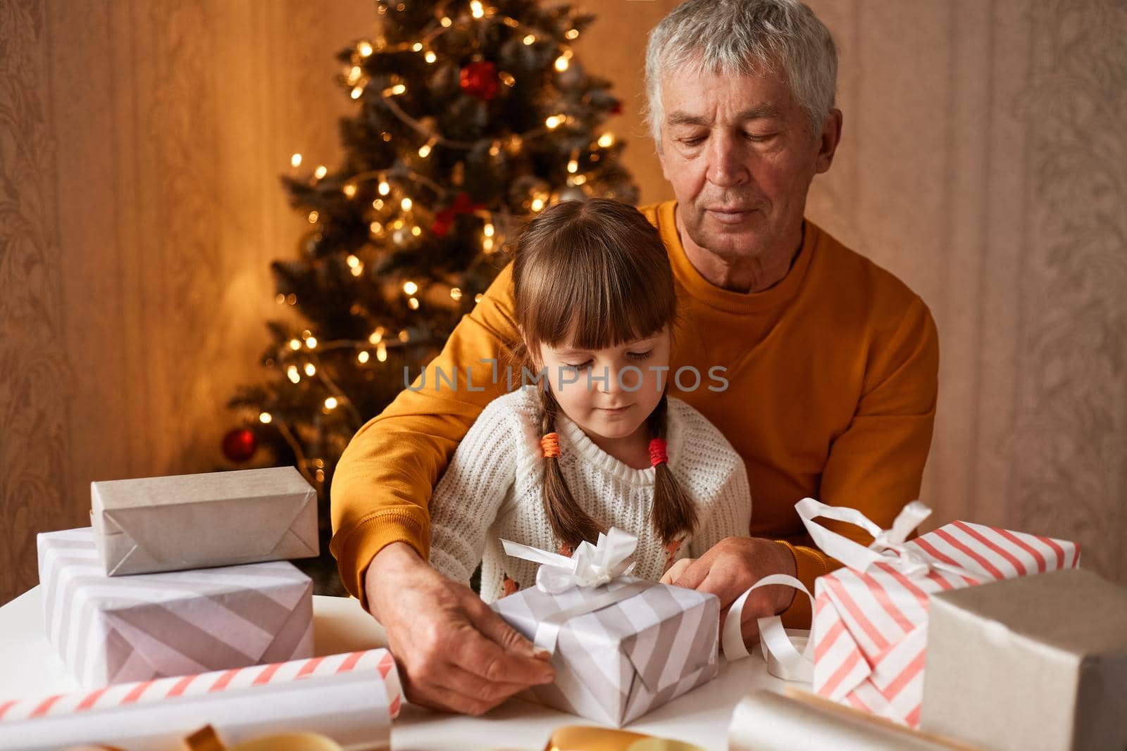Portrait of happy family wearing casual clothing sitting at table and preparing for new year eve, packing gift boxes together, posing in festive room with christmas tree.