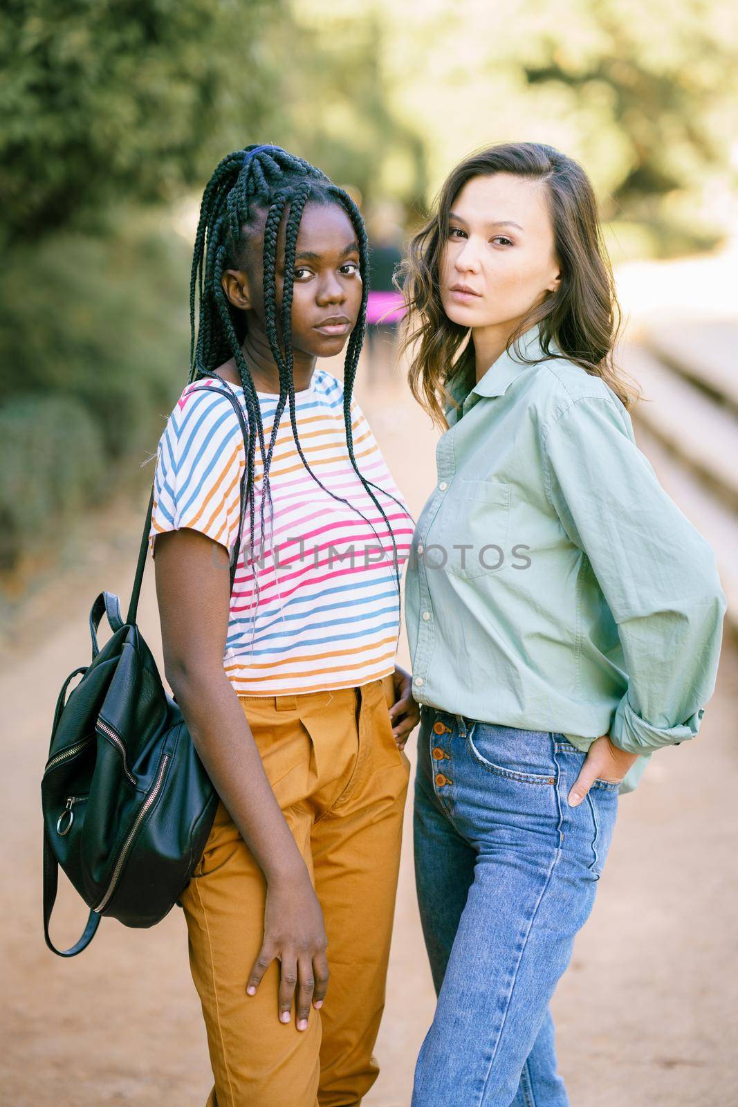 Two young friends looking at camera together on the street. Multiethnic women.