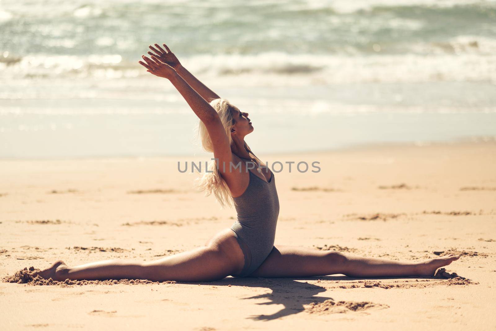 Caucasian woman practicing yoga at seashore. Young female doing fitness legs split on sand in the beach in Cadiz, Andalusia, Spain.