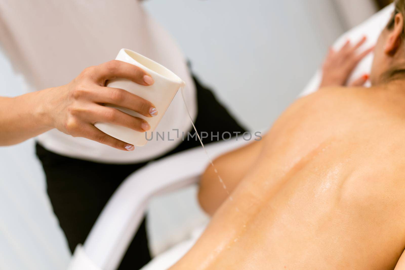 Beauty salon professional pouring oil from a massage candle on the back of his female patient.