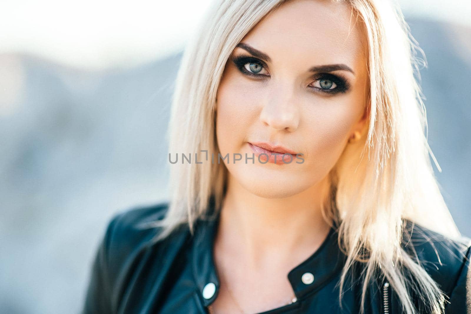 blonde girl in a black trouser suit with blue eyes on the background of a granite quarry from gray rubble