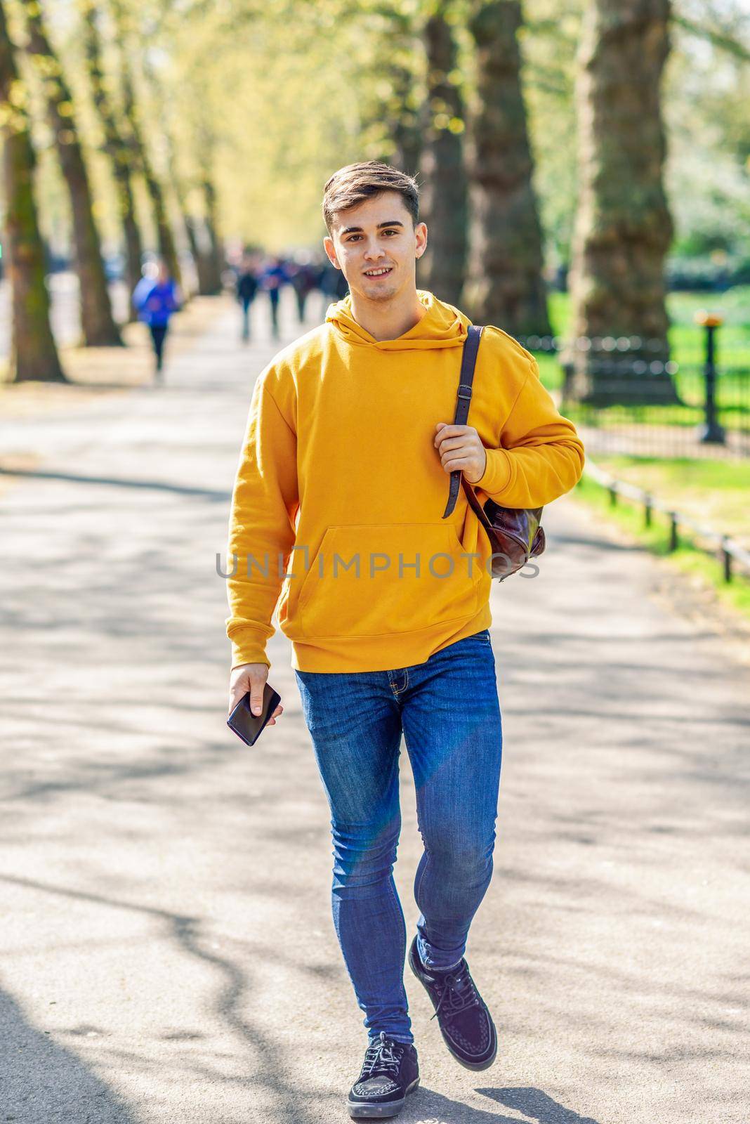 Young urban man using smartphone walking in street in an urban park in London, UK.