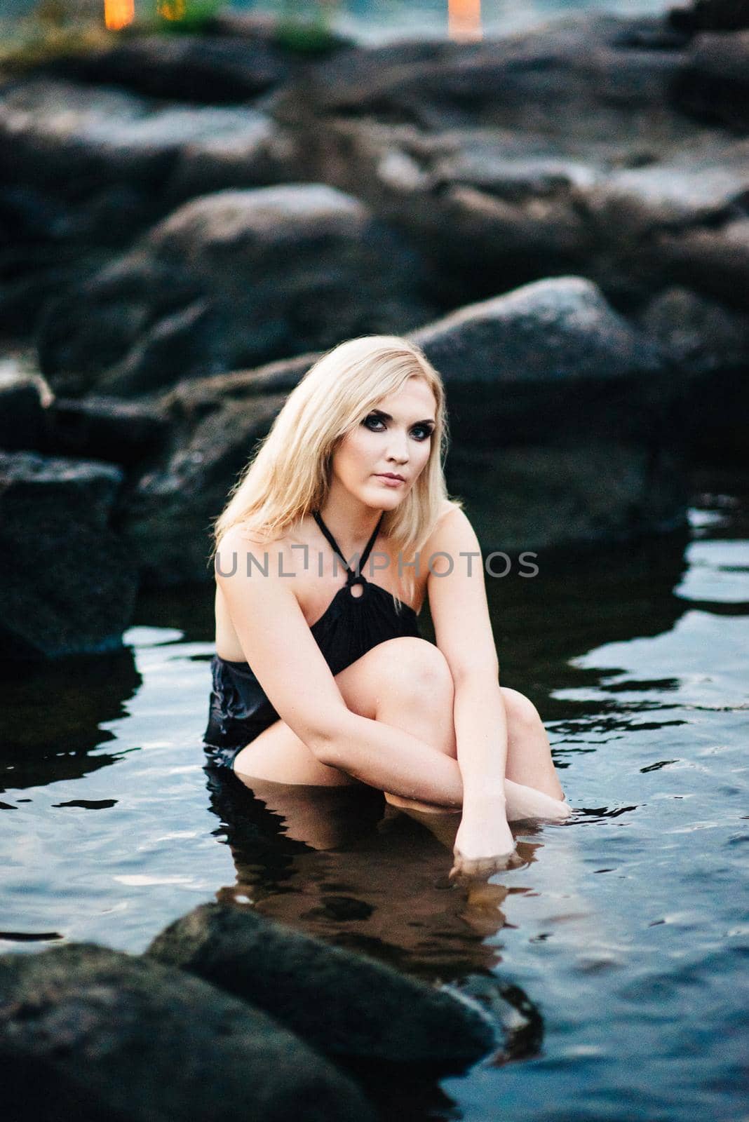 blonde girl in a black dress with blue eyes on the stone coast of the river