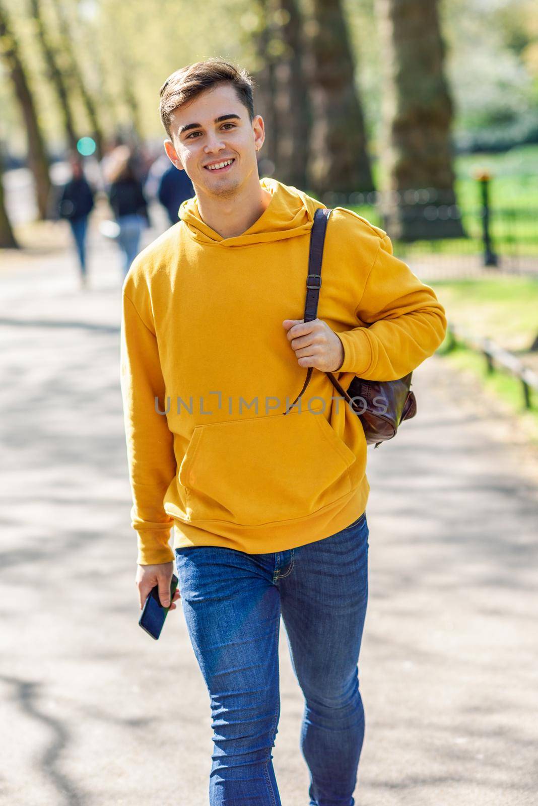 Young urban man using smartphone walking in street in an urban park in London, UK.