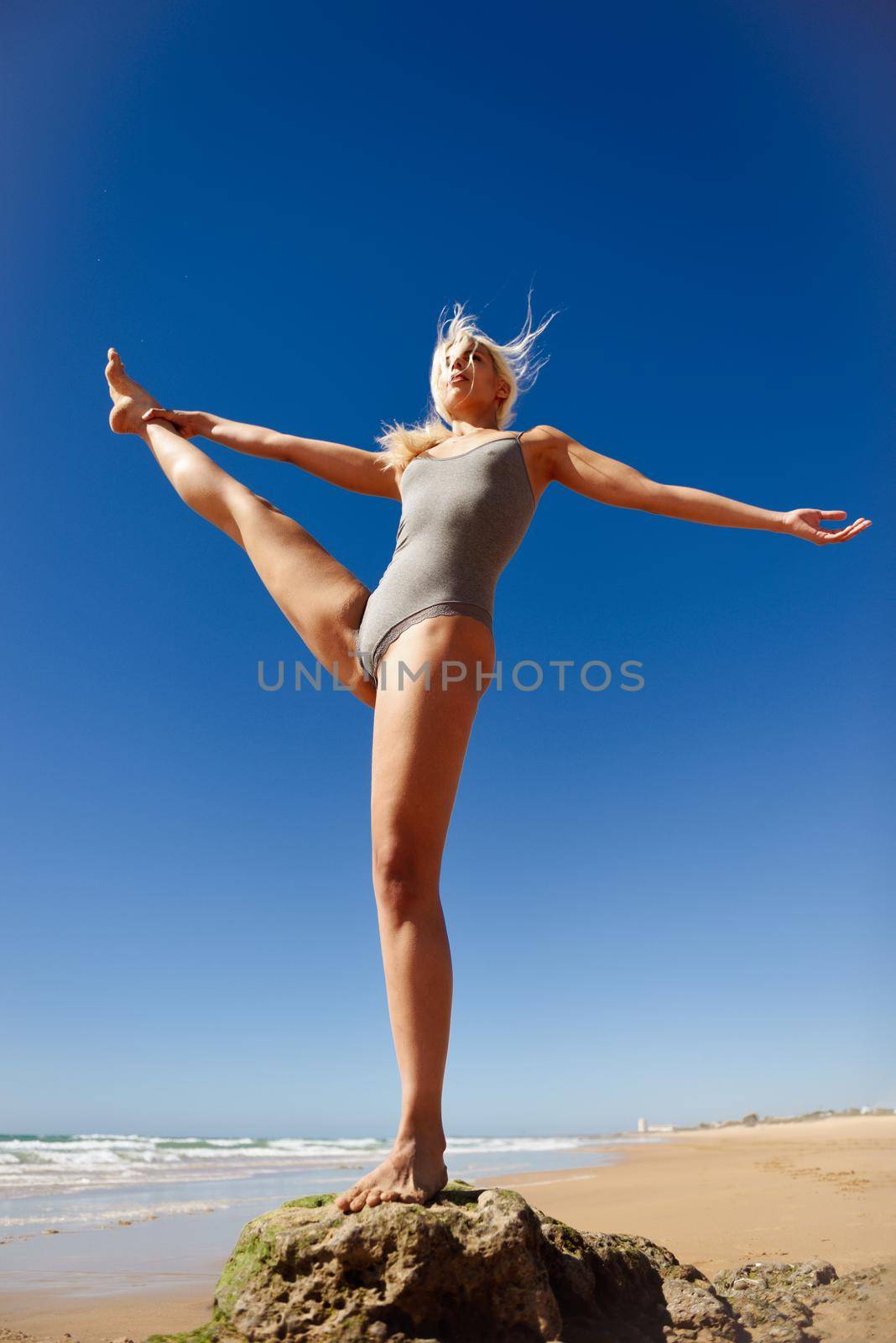 Caucasian woman practicing yoga at seashore. Young female standing on one leg while practicing the tree pose on a tranquil beach in Cadiz, Andalusia, Spain.