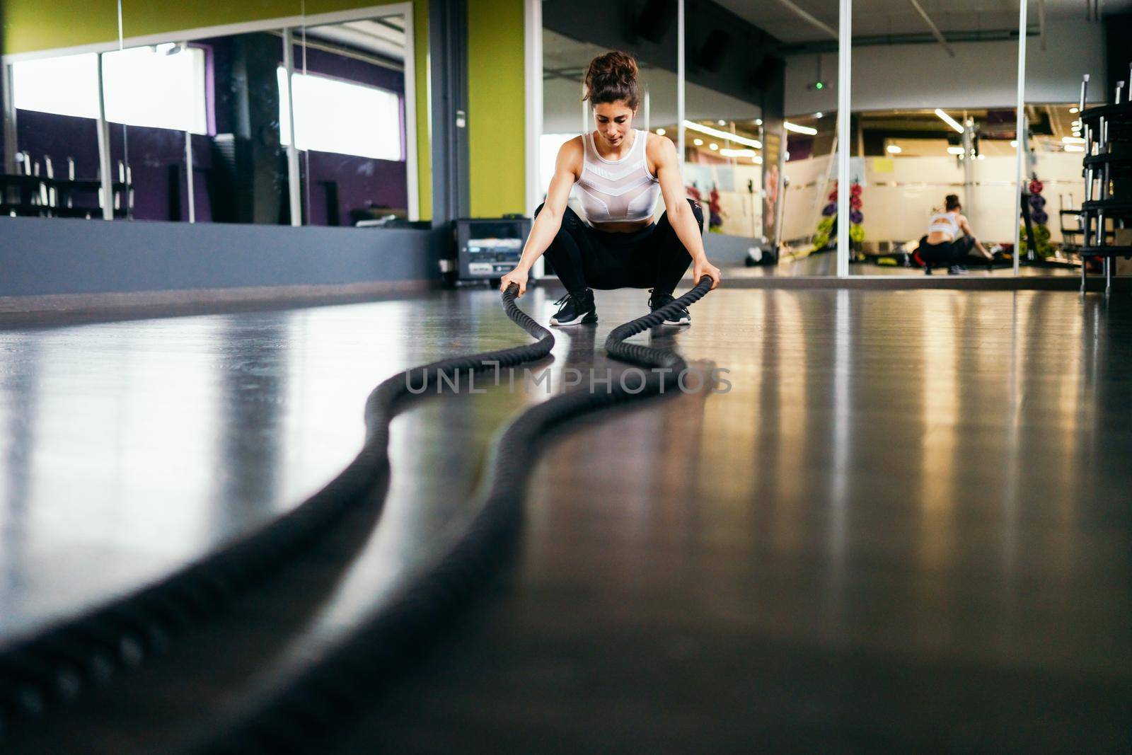 Young and athletic woman using training ropes in a gym. Fitness concept.