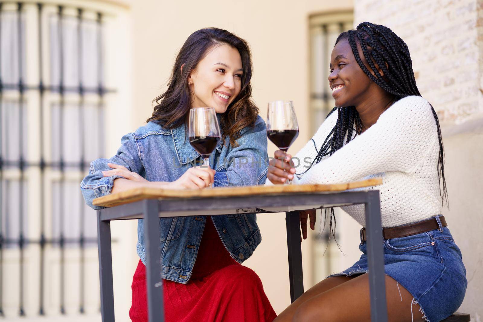 Two women drinking red wine sitting at a table outside a bar. by javiindy