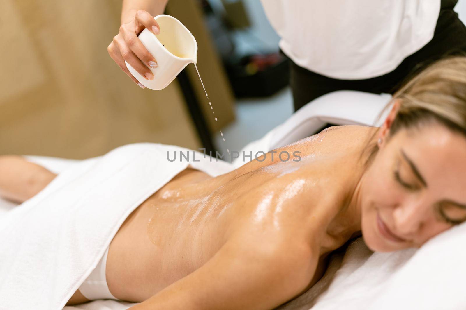 Beauty salon professional pouring oil from a massage candle on the back of his female patient.