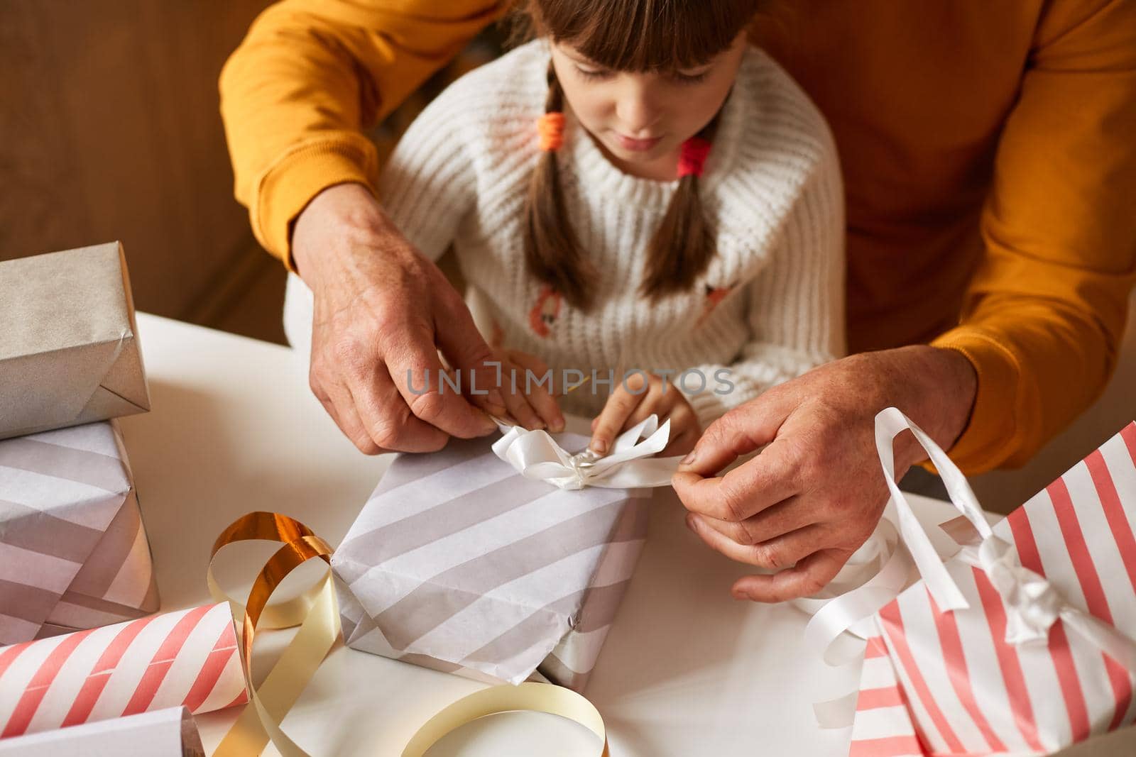 Portrait of little girl with pigtails posing with unrecognizable person and packing Christmas presents, wearing casual style clothing, happy new year.