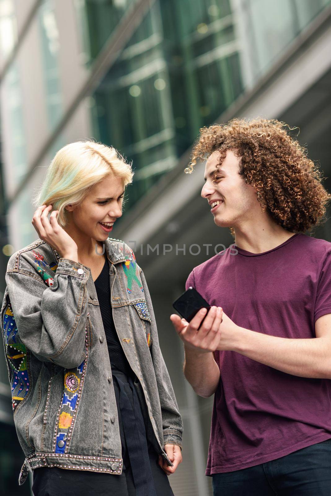 Happy couple using smartphone in urban background. Young man and woman wearing casual clothes in a London street.