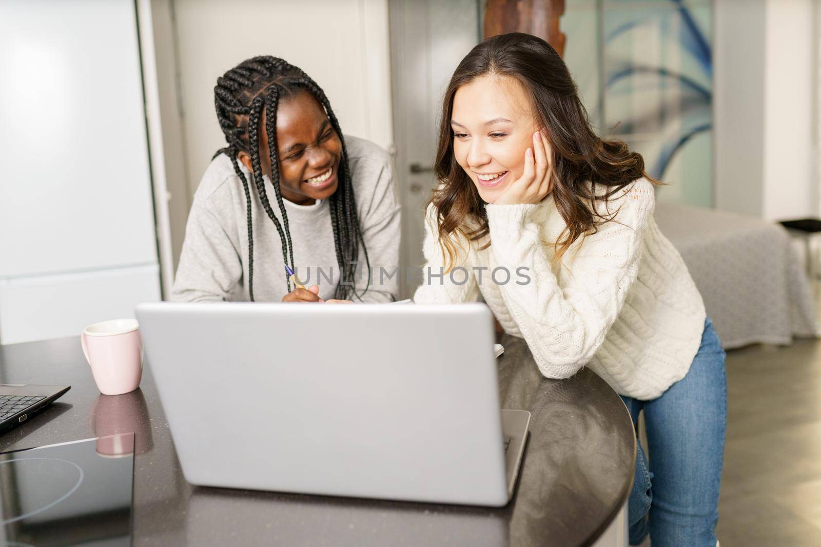 Two college girls studying together at home with laptops while drinking coffee. Multiethnic women.