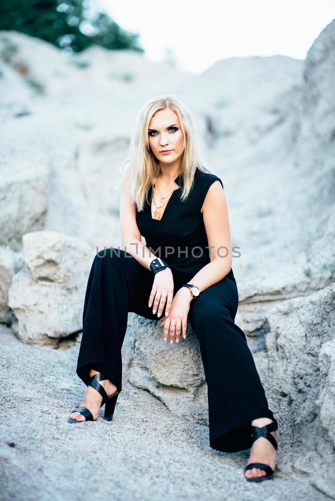 blonde girl in a black trouser suit with blue eyes on the background of a granite quarry from gray rubble