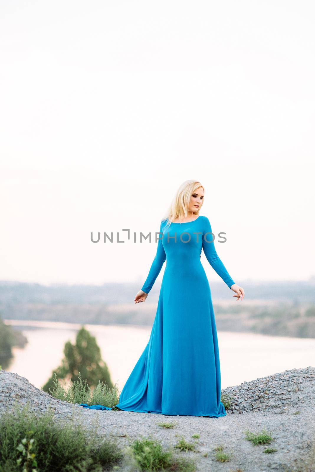 blonde girl in a blue dress with blue eyes in a granite quarry against the background of gravel