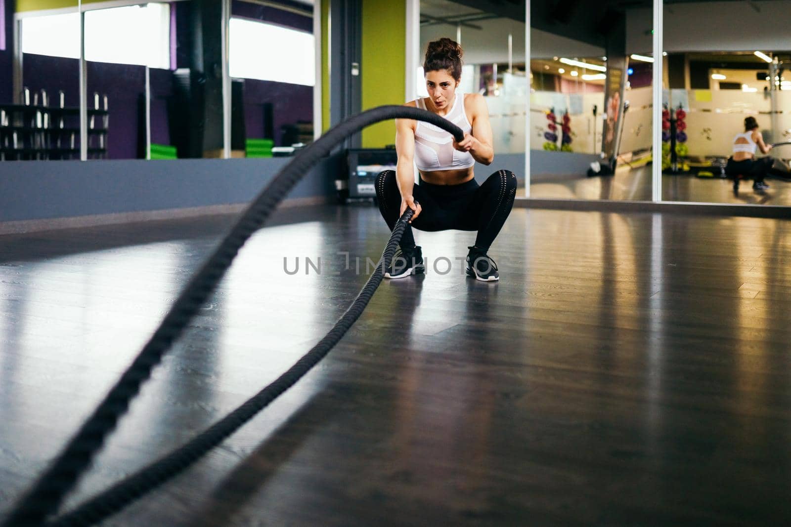 Young and athletic woman using training ropes in a gym. Fitness concept.