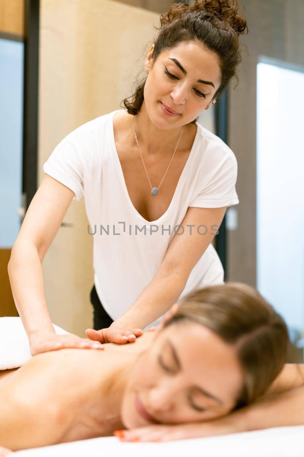 Female masseuse giving a back massage to a woman in a beauty parlour. by javiindy