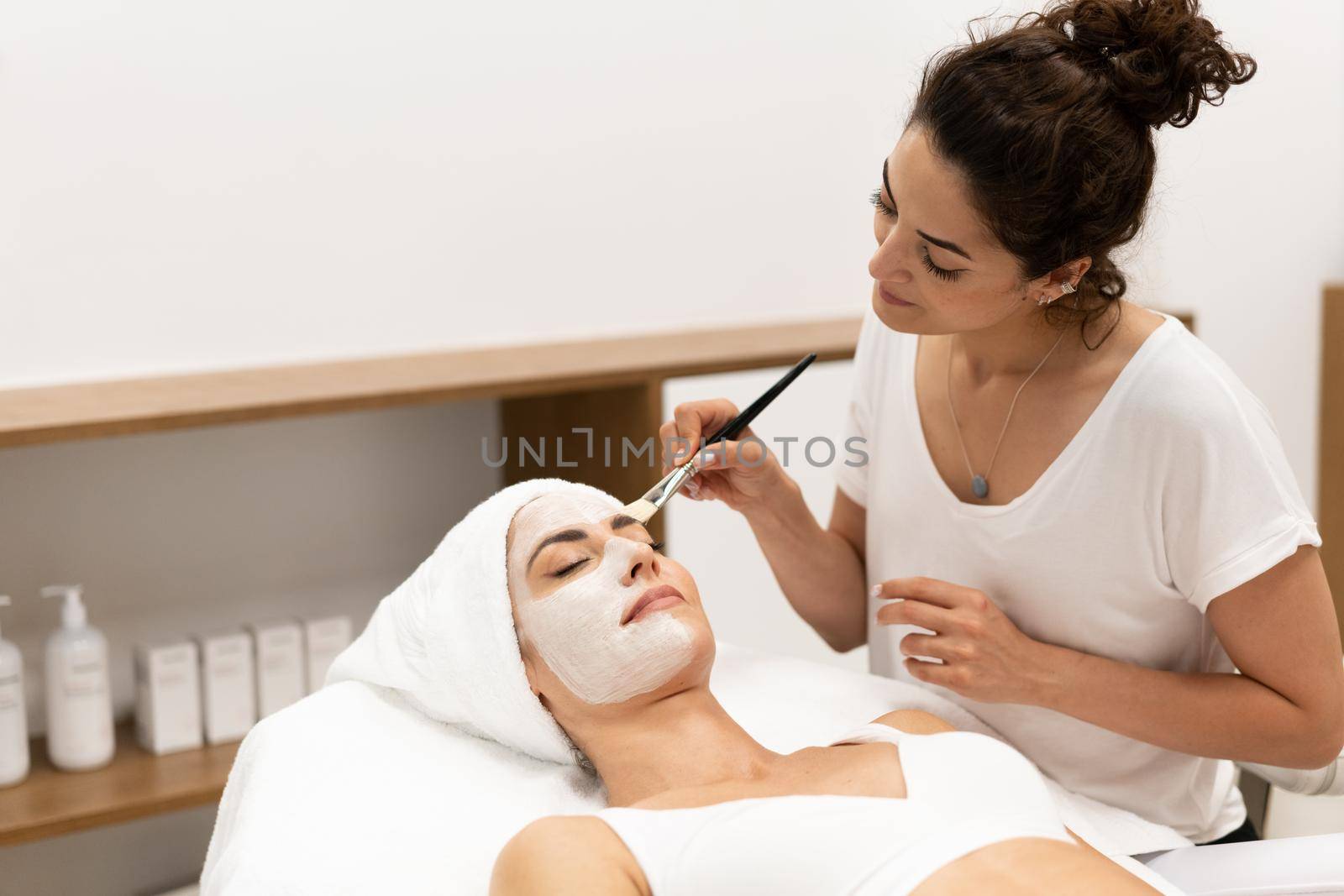 Aesthetics applying a mask to the face of a Middle-aged woman in modern wellness center. Beauty and Aesthetic concepts.