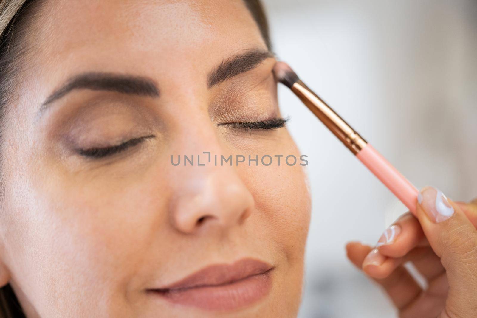 Close-up of a make-up artist applying eye shadow to her client. Beauty and Aesthetic concepts.