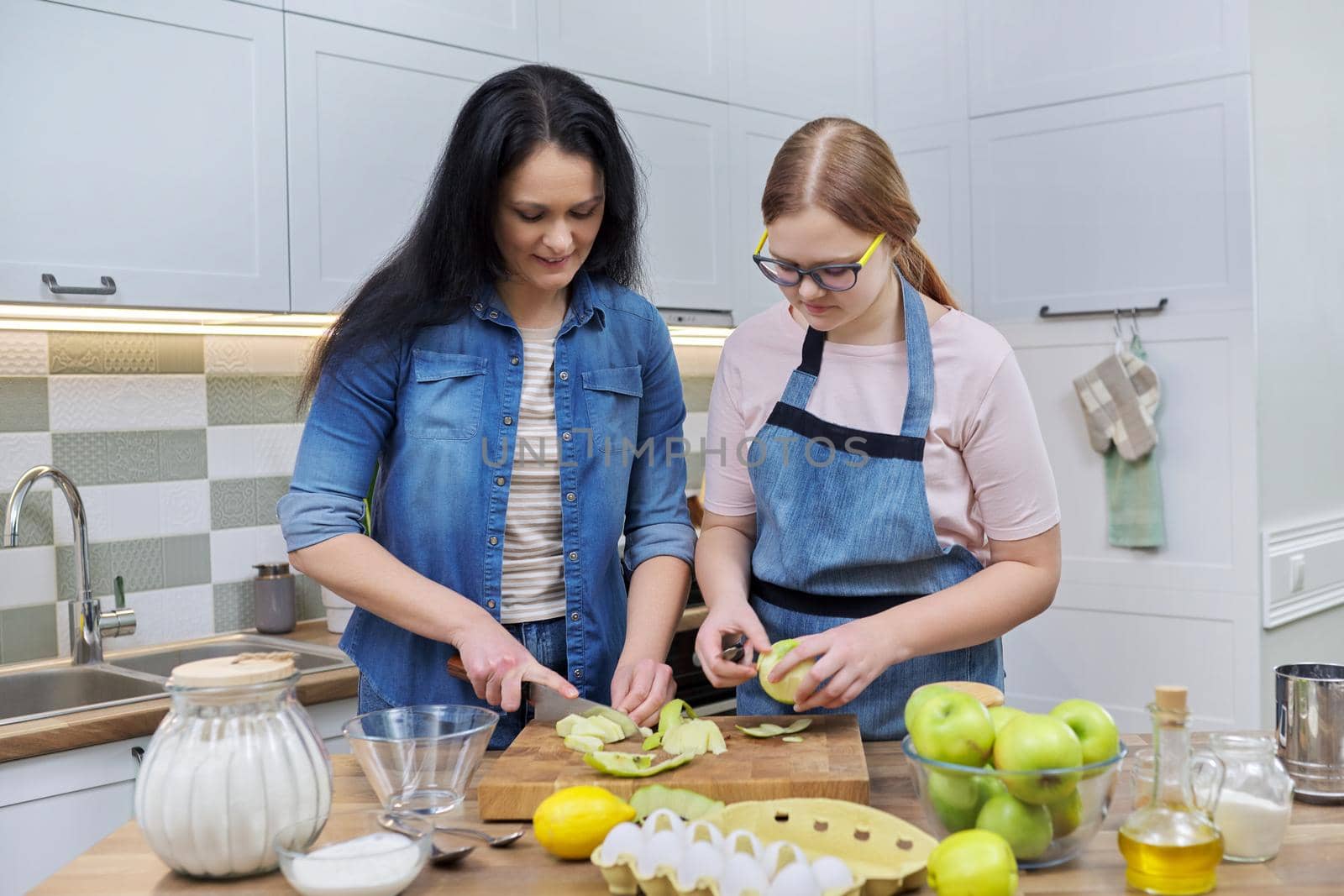 Family, relationships, lifestyle. Mom and teen daughter cooking apple pie together at home kitchen