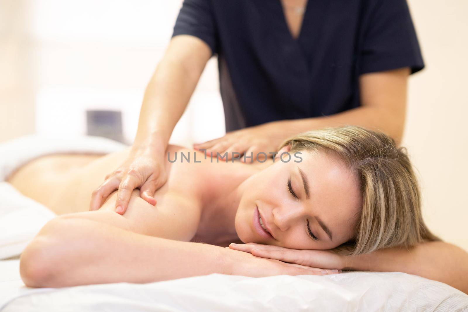 Young woman lying on a stretcher receiving a back massage in a physiotherapy center.