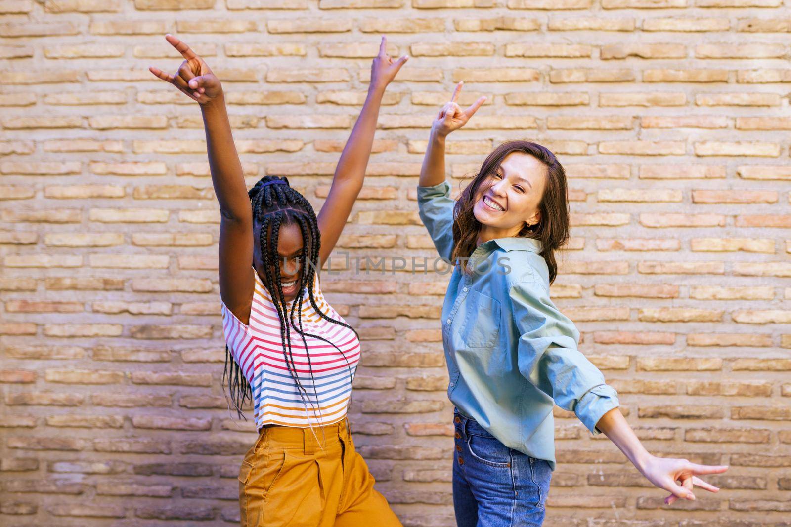 Two multiethnic women having fun together showing sign of the horns. by javiindy