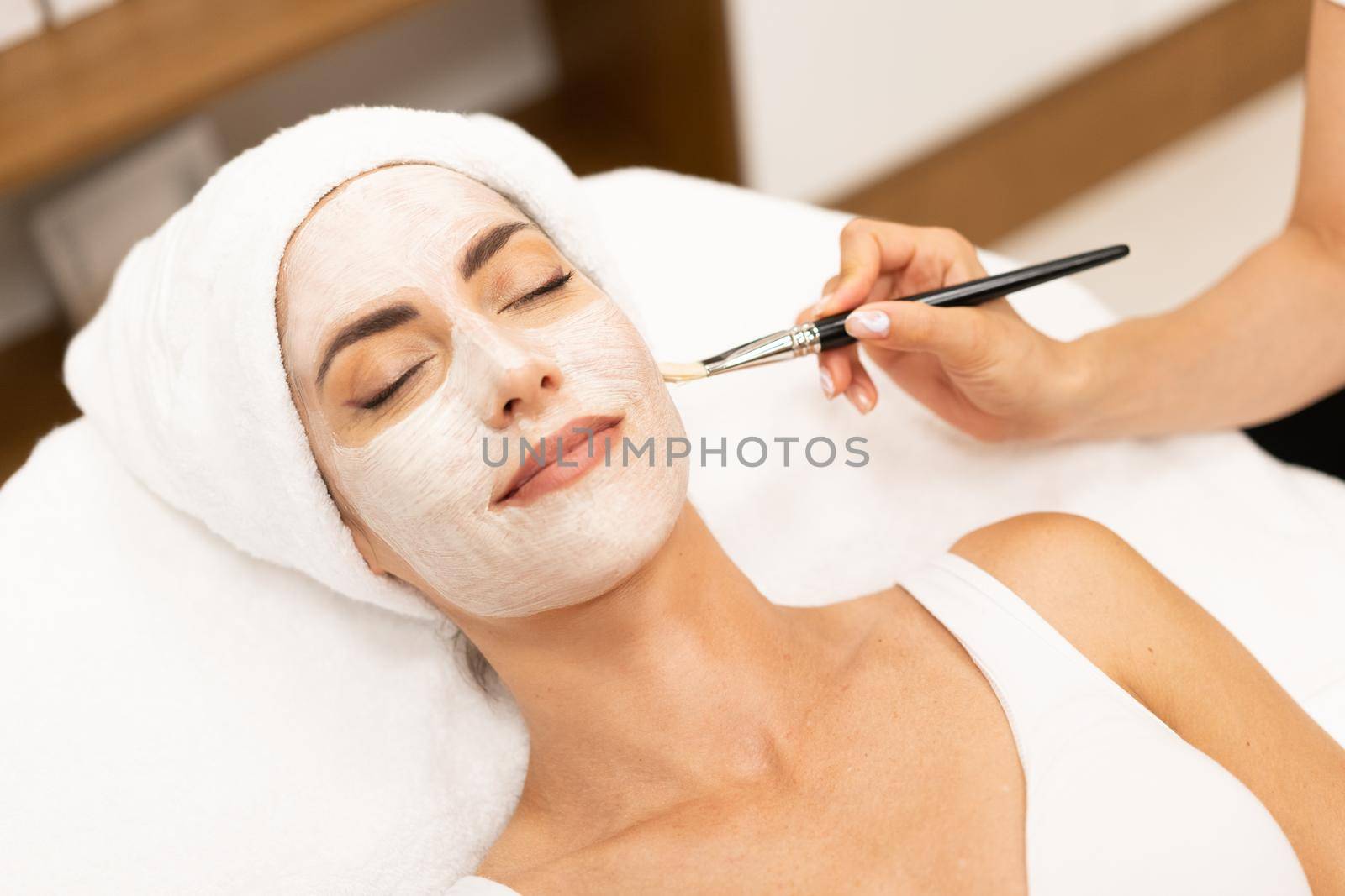 Aesthetics applying a mask to the face of a Middle-aged woman in modern wellness center. Beauty and Aesthetic concepts.