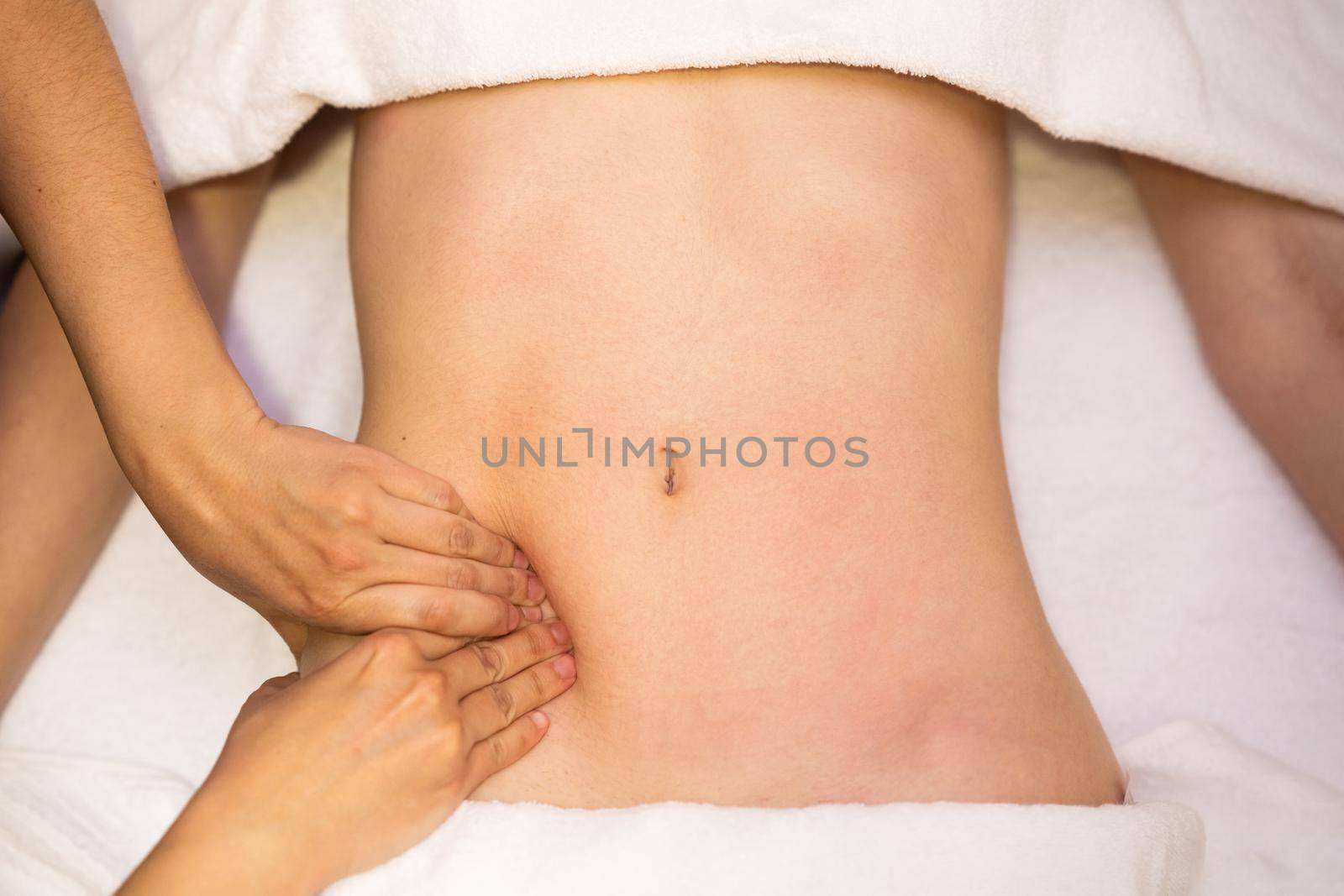 Top view of hands massaging female abdomen in a physiotherapy center. Therapist applying pressure on belly