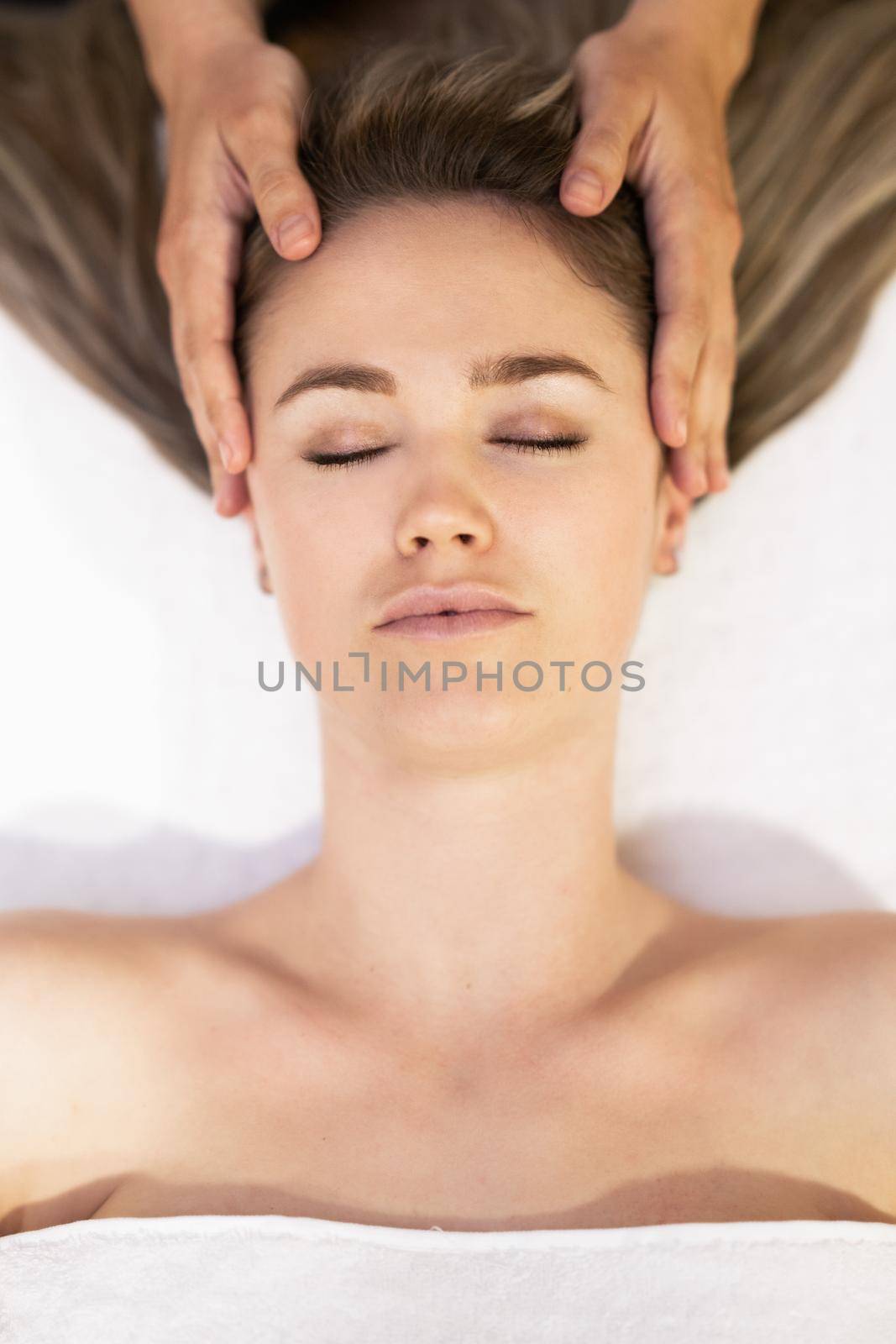 Young woman receiving a head massage in a spa center. Female patient is receiving treatment by professional therapist.