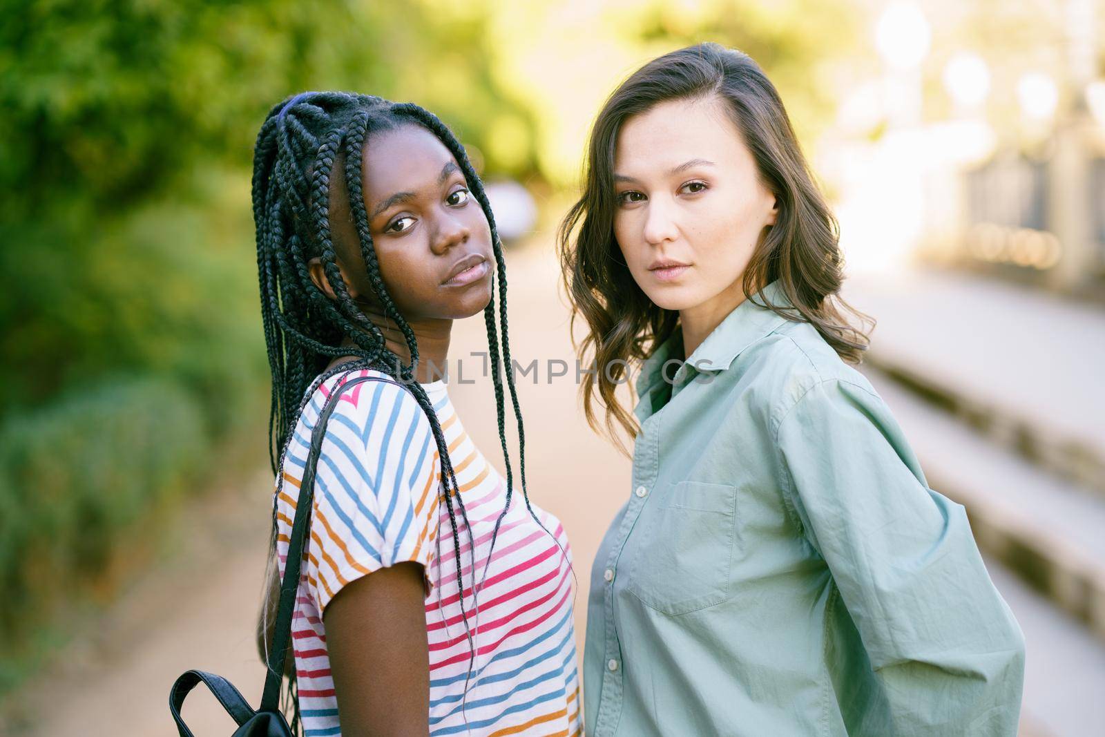 Two young friends looking at camera together on the street. Multiethnic women. by javiindy