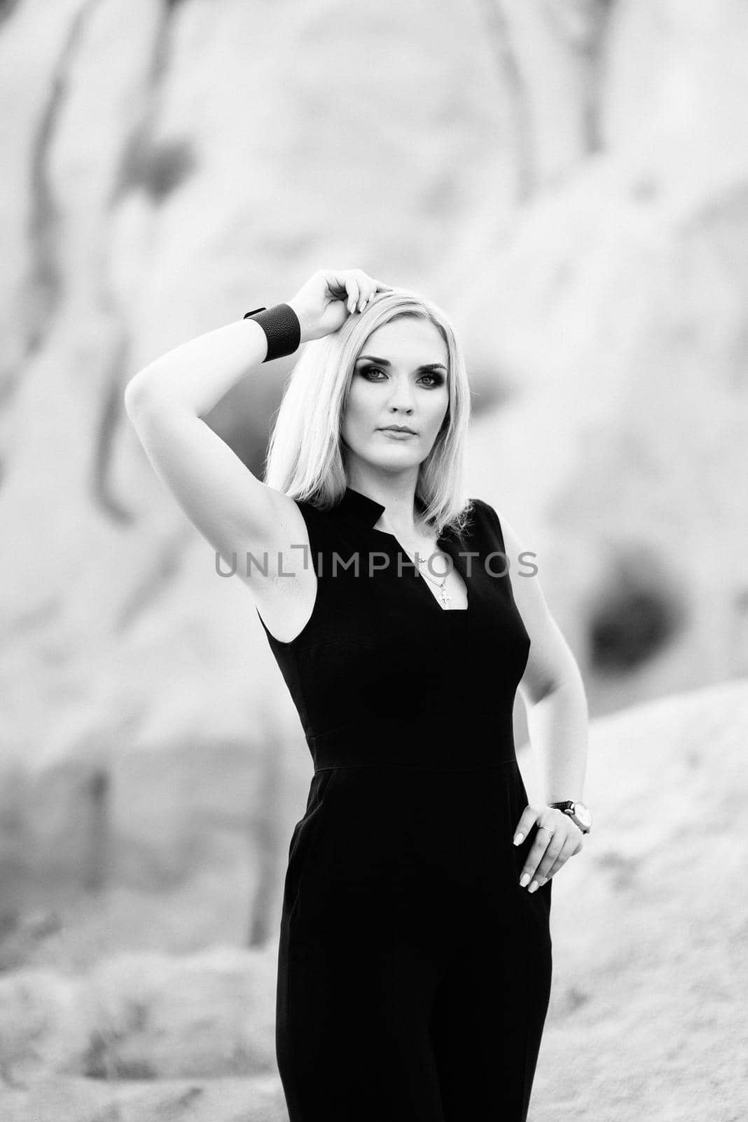 blonde girl in a black trouser suit with blue eyes on the background of a granite quarry from gray rubble