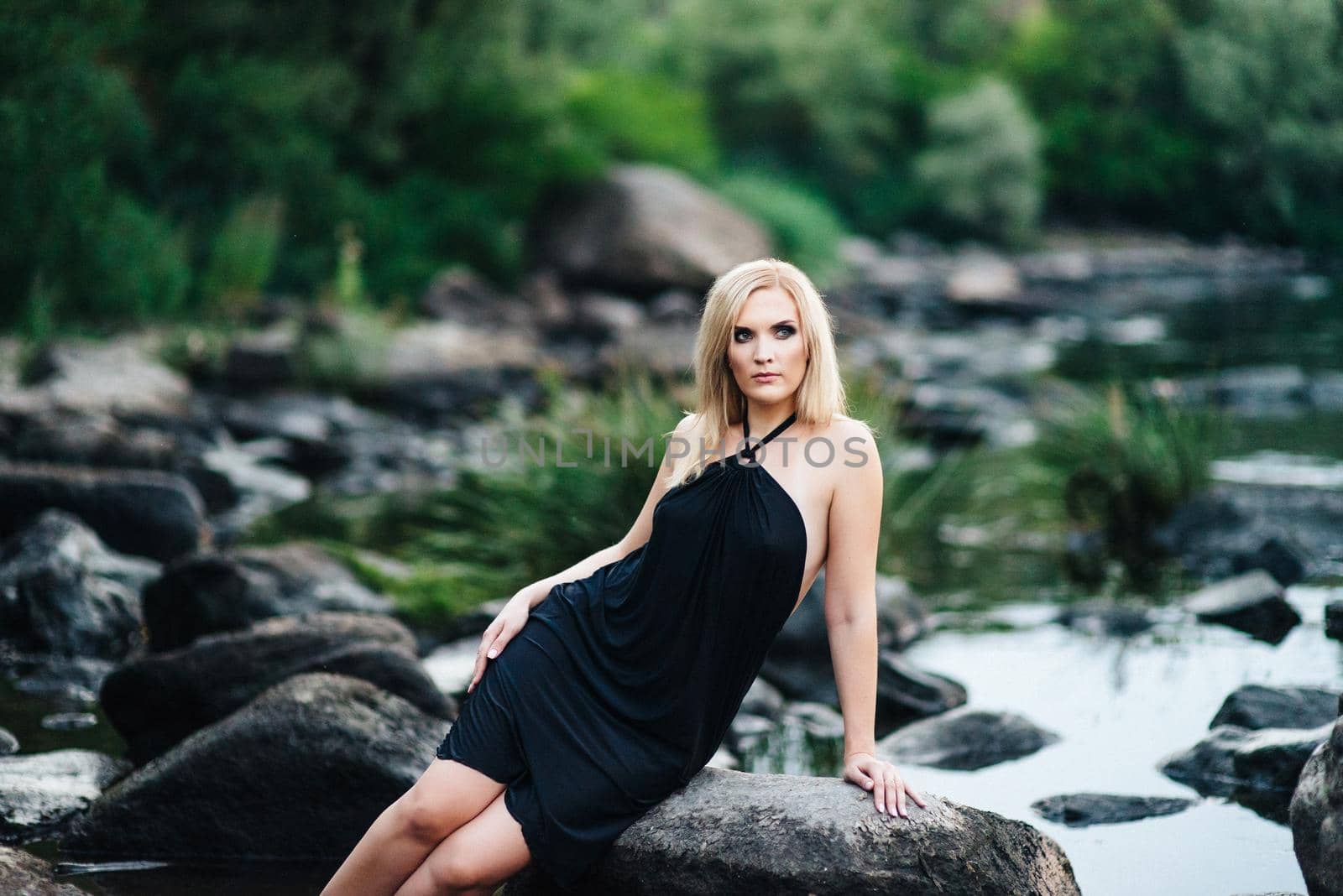 blonde girl in a black dress with blue eyes on the stone coast of the river