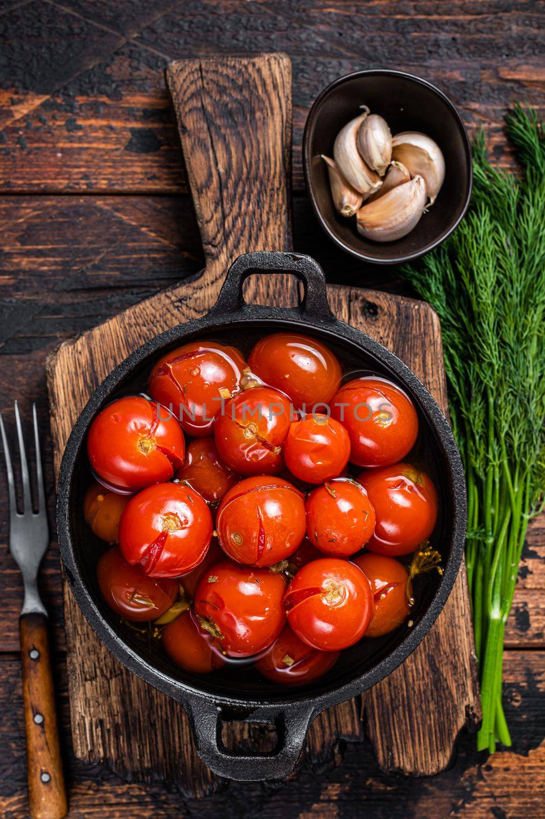 Salted Pickled cherry tomatoes in a pan with herbs and dill. Dark wooden background. Top view.