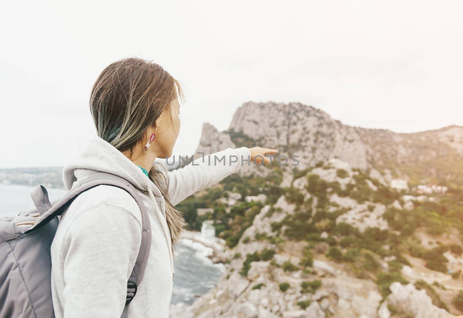 Backpacker young woman pointing at cliff on coastline. Image with sunlight effect.