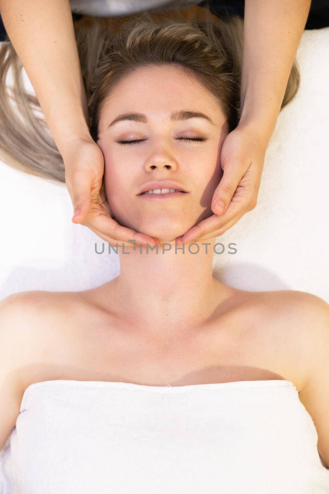 Young woman receiving a head massage in a spa center. Female patient is receiving treatment by professional therapist.