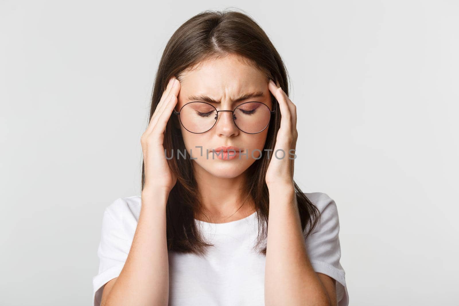 Close-up of young woman in glasses touching head and grimacing from pain, having headache or migraine, feeling sick.