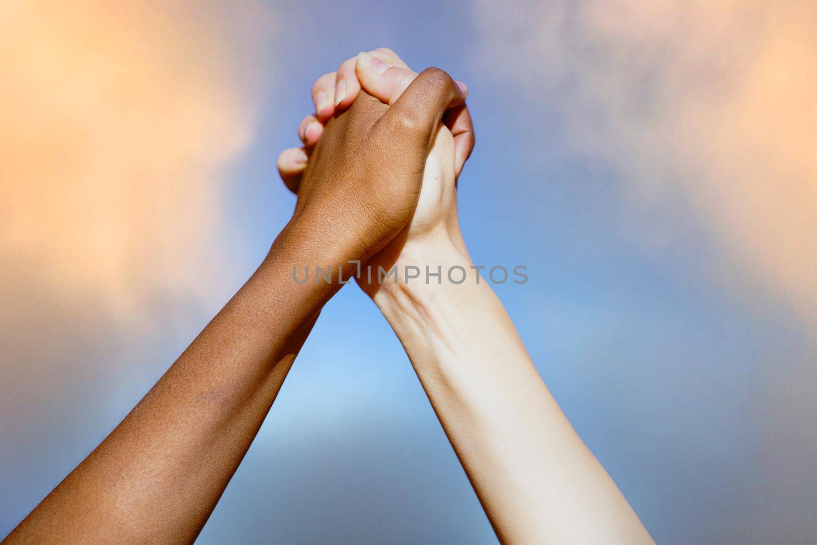 Close up of multiethnic women's hands together against cloudy sky.