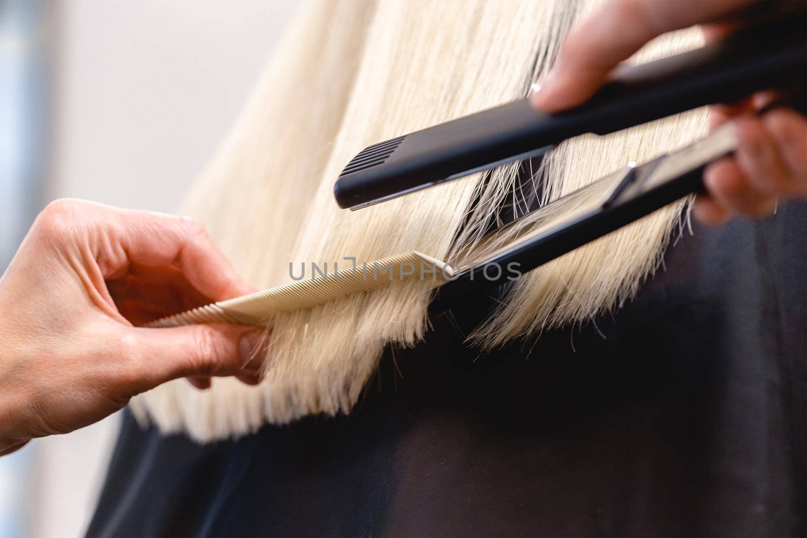 Hairdresser using a flat iron hair straightener to straighten woman's blonde hair