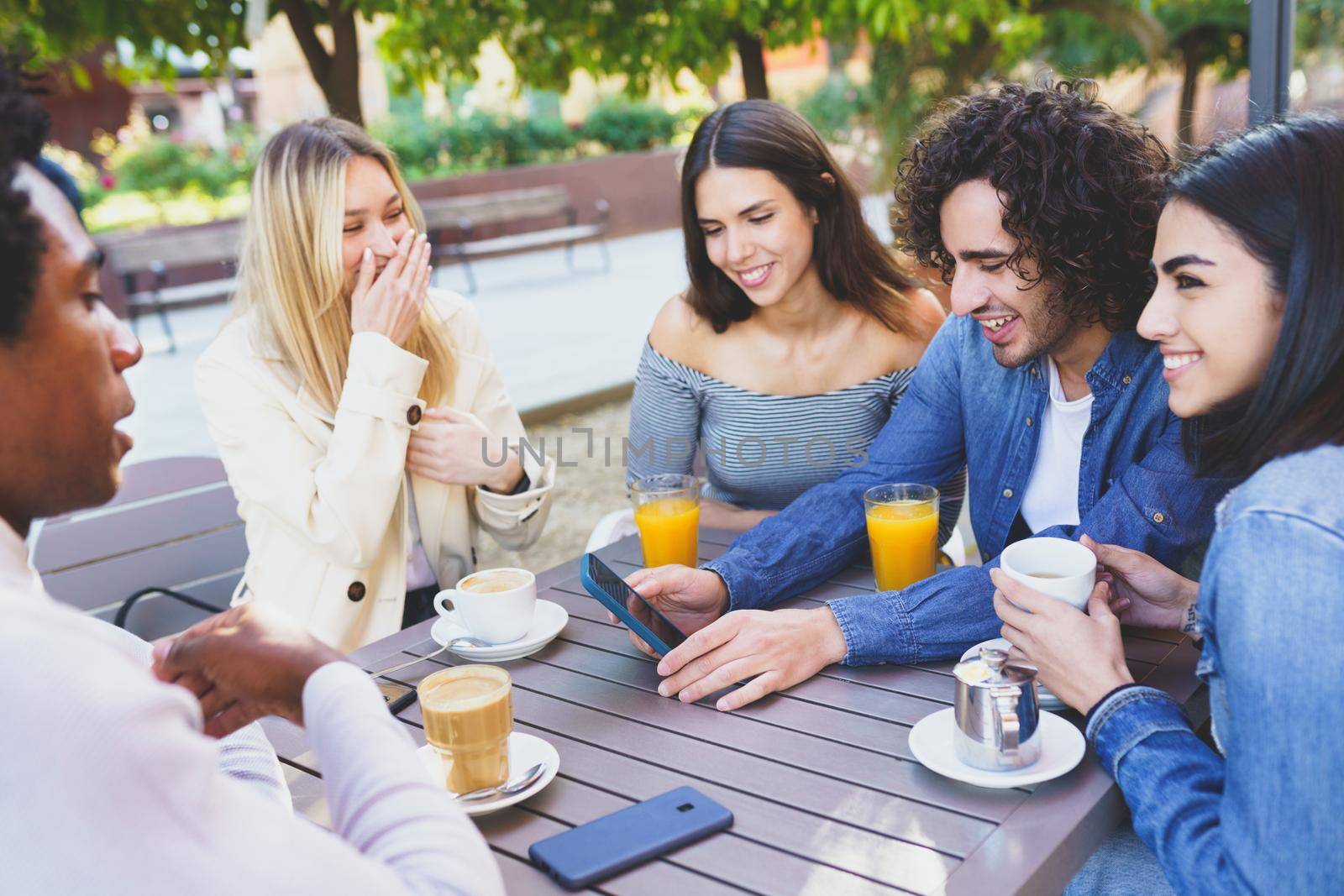 Multi-ethnic group of students having a drink on the terrace of a street bar. Young people having fun together