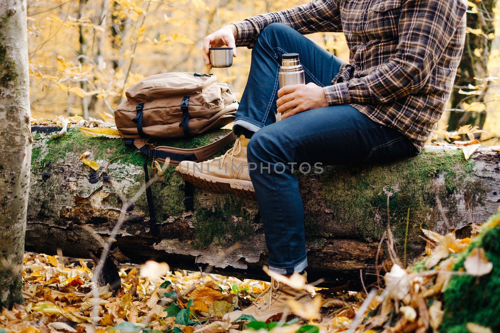 Unrecognizable young man resting with cup of tea in autumn forest.